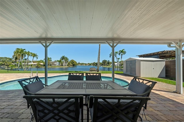 view of patio featuring a fenced in pool, a water view, an outbuilding, outdoor dining space, and a storage unit