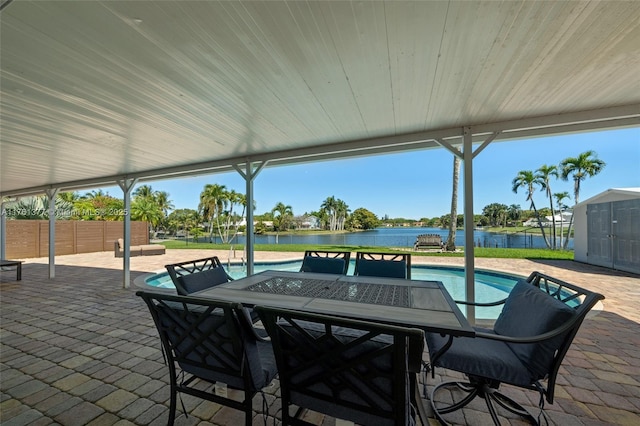 view of patio featuring an outdoor pool, a water view, outdoor dining space, and fence