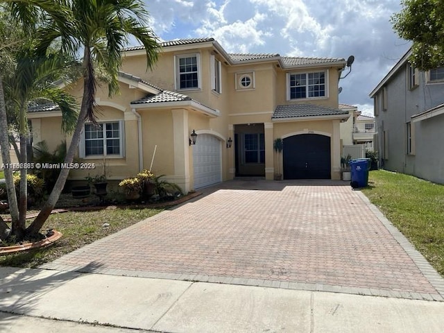 mediterranean / spanish home with stucco siding, a tiled roof, decorative driveway, and a garage