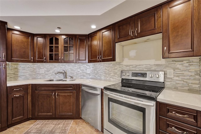 kitchen featuring a sink, light countertops, glass insert cabinets, appliances with stainless steel finishes, and backsplash