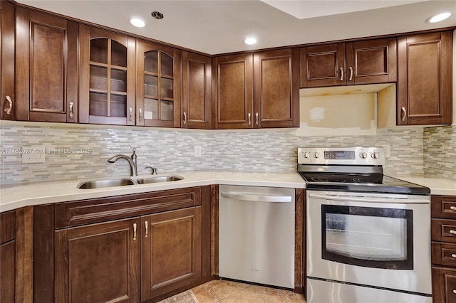 kitchen featuring a sink, decorative backsplash, light countertops, glass insert cabinets, and appliances with stainless steel finishes