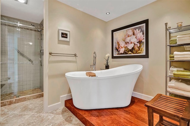 full bath featuring a shower stall, a freestanding bath, and baseboards