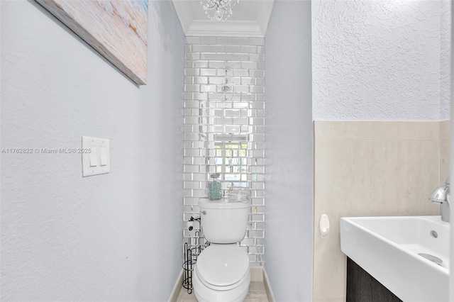 half bath featuring toilet, a sink, crown molding, a notable chandelier, and tile walls