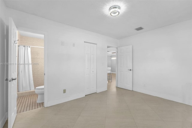 unfurnished bedroom featuring light tile patterned floors, baseboards, visible vents, a closet, and connected bathroom