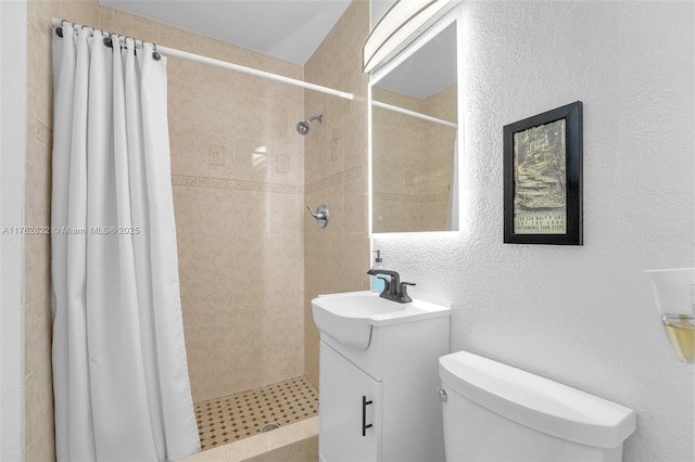 bathroom with toilet, tiled shower, vanity, and a textured wall