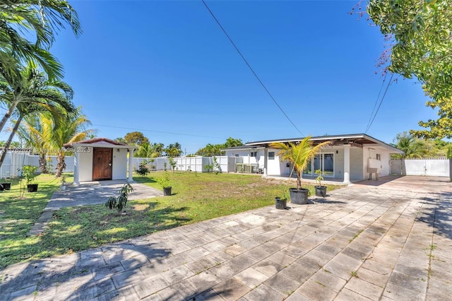 view of front facade with a front lawn, an outdoor structure, a fenced backyard, a storage unit, and a patio