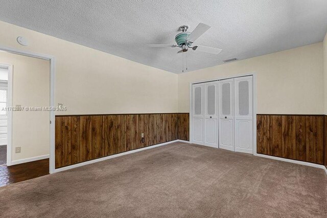 unfurnished bedroom with a textured ceiling, wood walls, and wainscoting