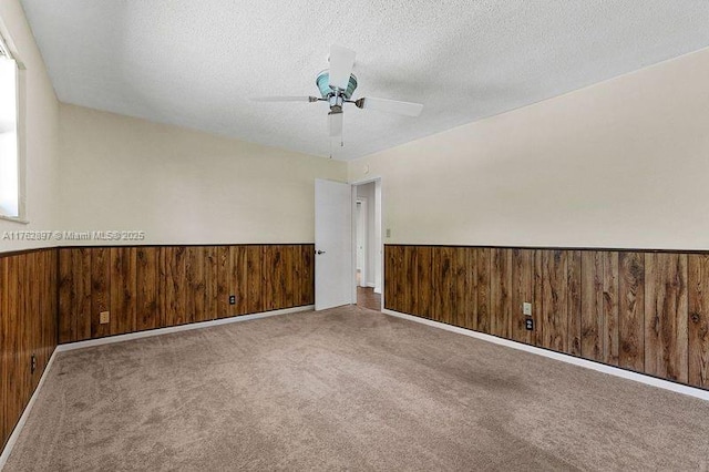 empty room featuring carpet flooring, a textured ceiling, wood walls, and wainscoting