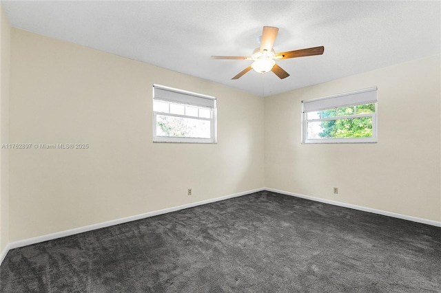 empty room featuring dark colored carpet, a ceiling fan, baseboards, and a wealth of natural light