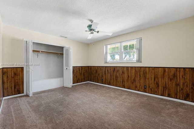 unfurnished bedroom with wooden walls, carpet, a wainscoted wall, a closet, and a textured ceiling