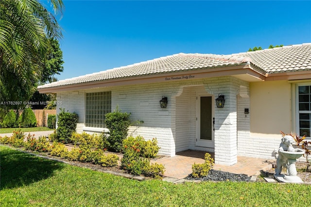 property entrance with a patio area, brick siding, and a tiled roof