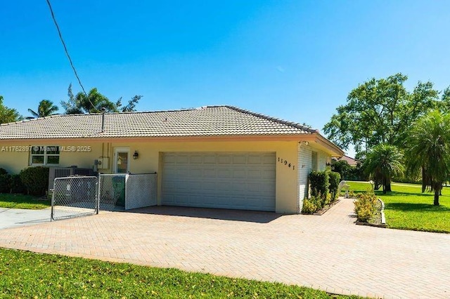 exterior space featuring a gate, an attached garage, stucco siding, a tiled roof, and decorative driveway