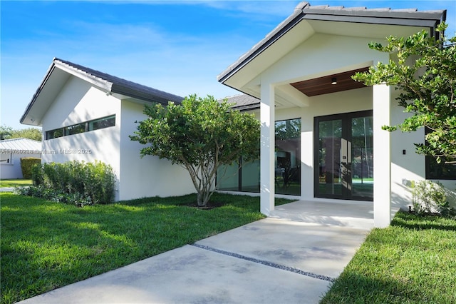 property entrance with french doors, a yard, and stucco siding