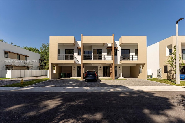 view of front of house with decorative driveway, fence, and stucco siding