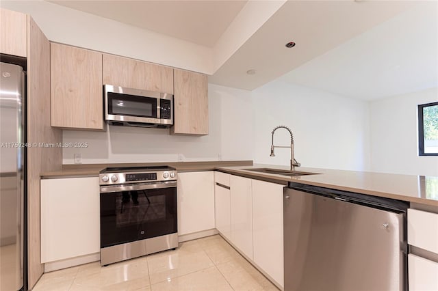 kitchen featuring light tile patterned floors, a sink, light brown cabinetry, stainless steel appliances, and modern cabinets