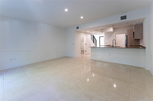 unfurnished living room featuring visible vents, stairs, baseboards, and a sink