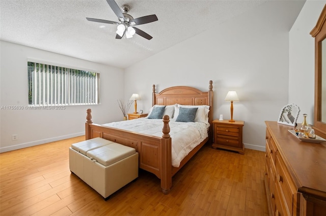 bedroom with lofted ceiling, a textured ceiling, light wood finished floors, baseboards, and ceiling fan