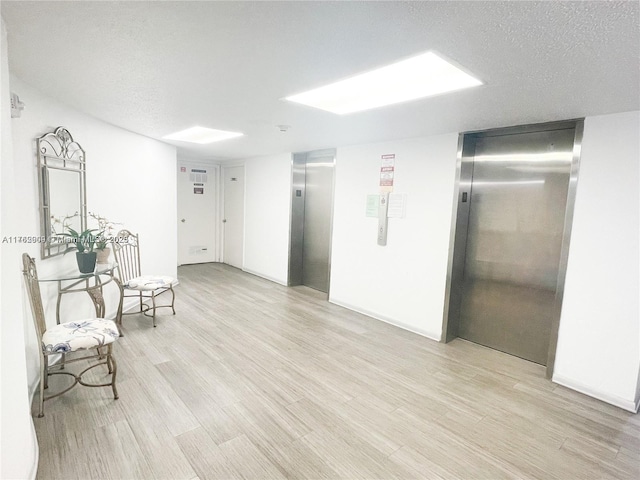 hallway with elevator, light wood-style flooring, and a textured ceiling