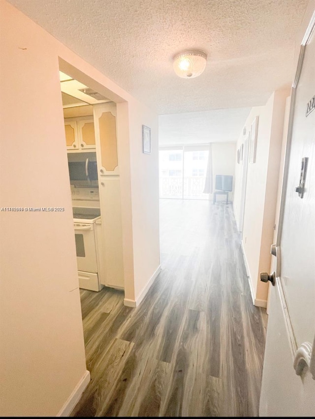 hallway featuring wood finished floors, baseboards, and a textured ceiling