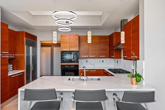 kitchen featuring a tray ceiling, a peninsula, black appliances, wall chimney exhaust hood, and a sink