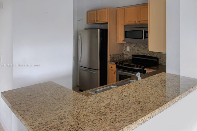 kitchen with light stone counters, a peninsula, a sink, decorative backsplash, and stainless steel appliances