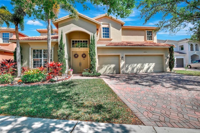 mediterranean / spanish-style home with a garage, stucco siding, decorative driveway, and a front lawn