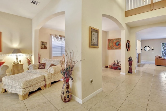 hallway featuring tile patterned floors, a high ceiling, arched walkways, and visible vents