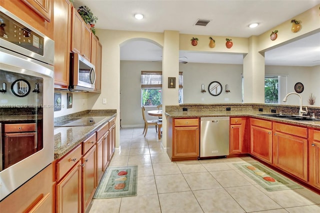 kitchen with light stone countertops, light tile patterned flooring, arched walkways, a sink, and appliances with stainless steel finishes