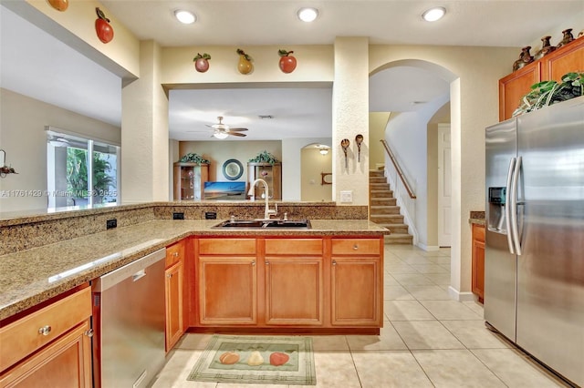 kitchen with brown cabinets, a sink, light stone counters, appliances with stainless steel finishes, and light tile patterned floors