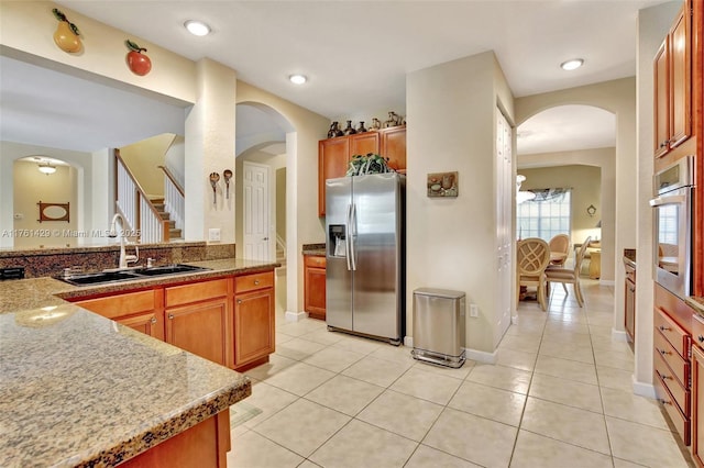 kitchen with brown cabinets, a sink, arched walkways, appliances with stainless steel finishes, and light tile patterned flooring