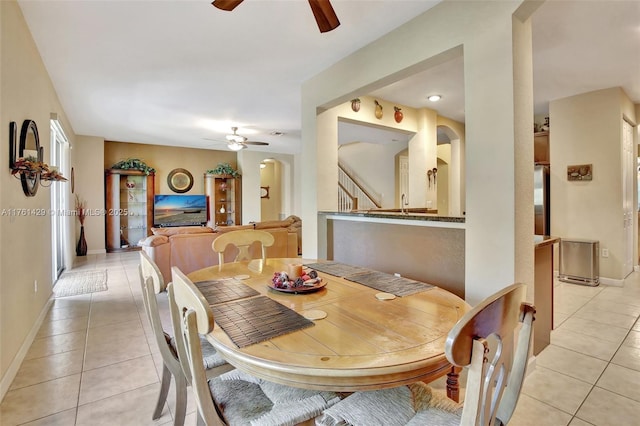 dining room featuring light tile patterned floors, baseboards, arched walkways, and a ceiling fan