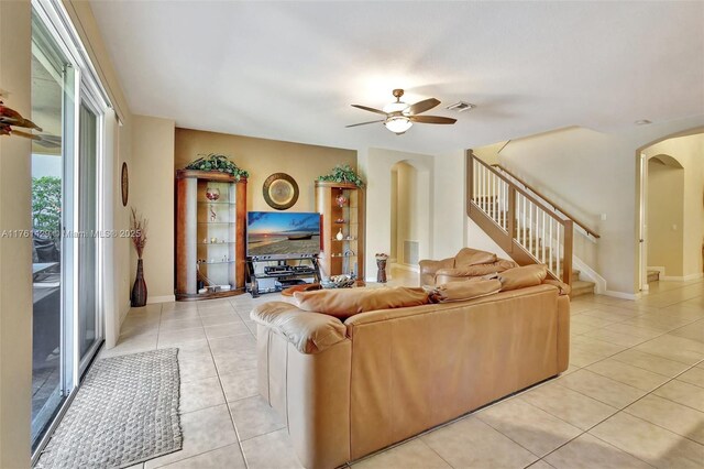 living room featuring visible vents, stairway, light tile patterned floors, arched walkways, and a ceiling fan