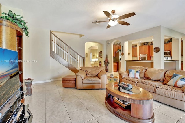 living area featuring light tile patterned floors, arched walkways, stairs, and ceiling fan