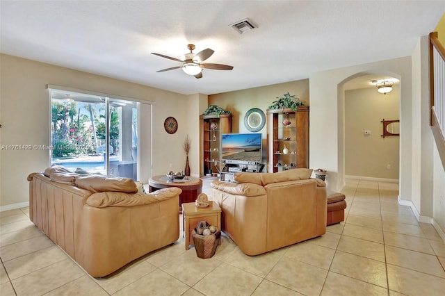 living room featuring light tile patterned floors, a ceiling fan, visible vents, baseboards, and arched walkways