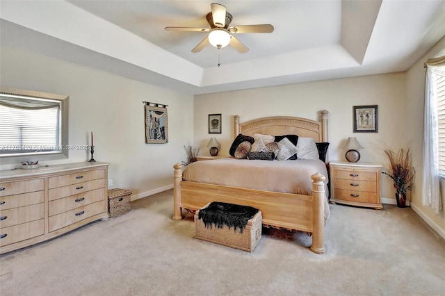 bedroom with baseboards, a raised ceiling, and light colored carpet