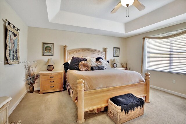 bedroom featuring a tray ceiling, baseboards, light colored carpet, and ceiling fan