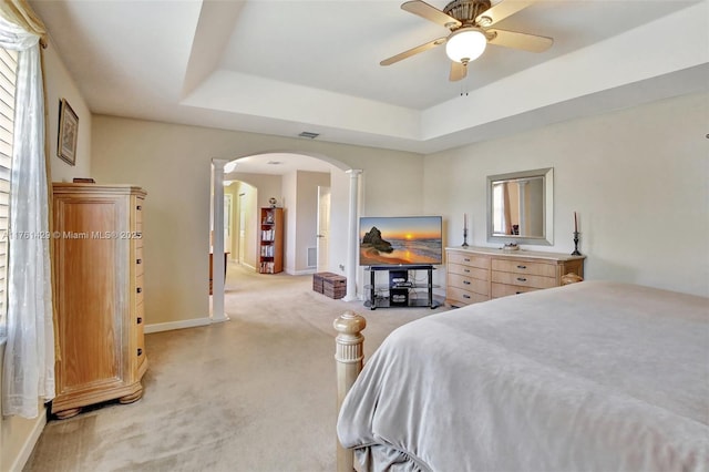 bedroom featuring a raised ceiling, visible vents, arched walkways, and light carpet