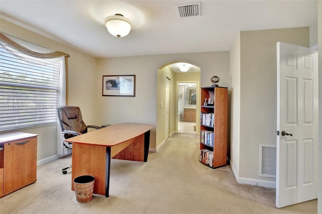 office area featuring light colored carpet, arched walkways, visible vents, and baseboards