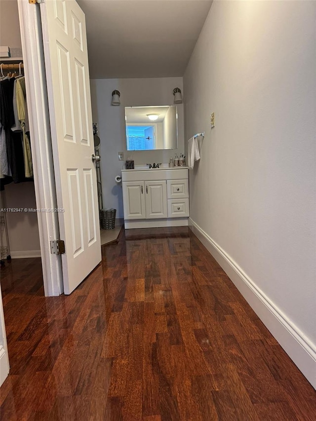 hallway with dark wood-style floors, baseboards, and a sink