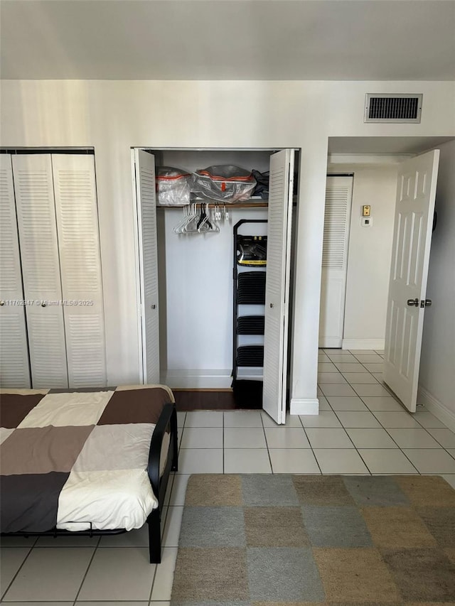 bedroom with light tile patterned floors, baseboards, visible vents, and multiple closets