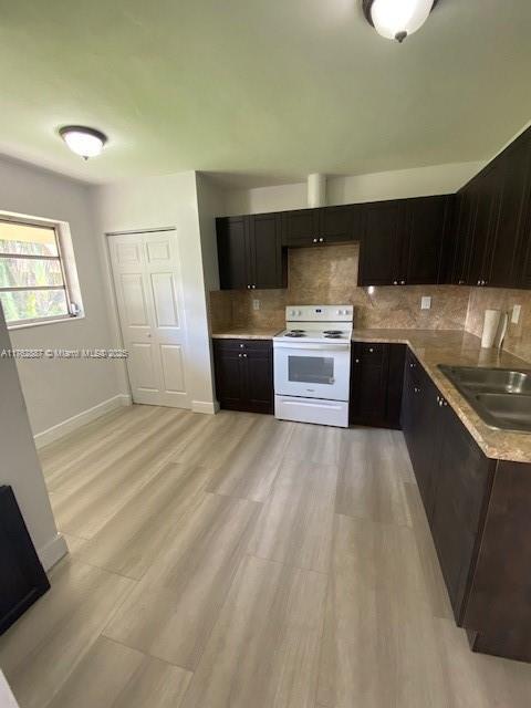 kitchen featuring electric range, light wood-style flooring, a sink, decorative backsplash, and baseboards