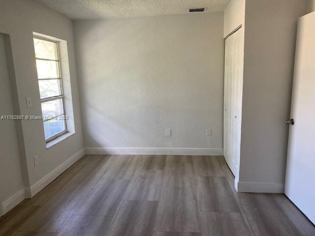 unfurnished room featuring visible vents, baseboards, a textured ceiling, and wood finished floors