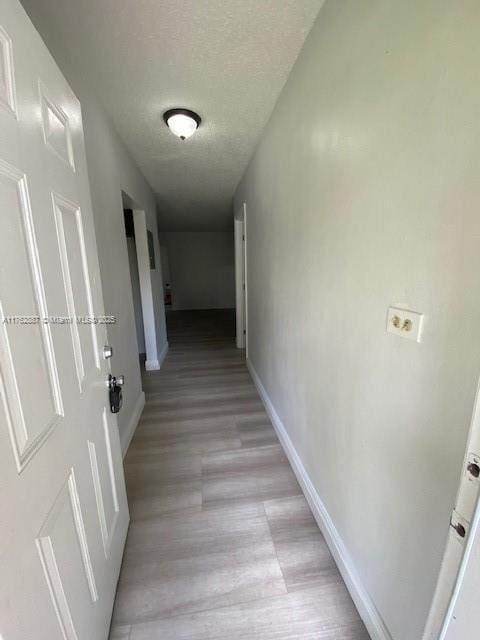 hallway with light wood finished floors, a textured ceiling, and baseboards