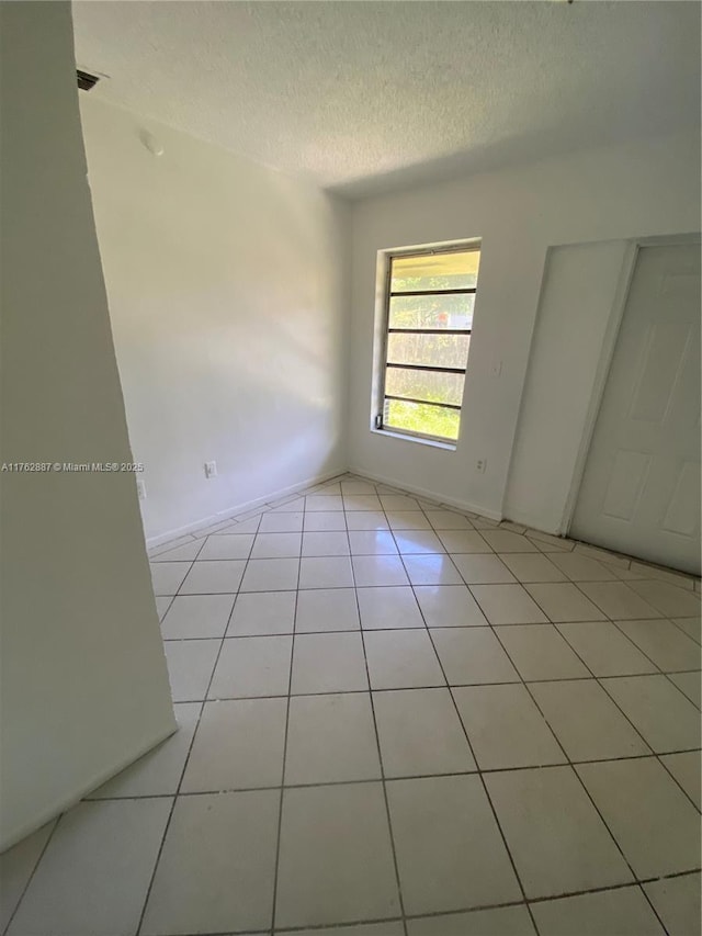 spare room featuring baseboards, a textured ceiling, and light tile patterned flooring