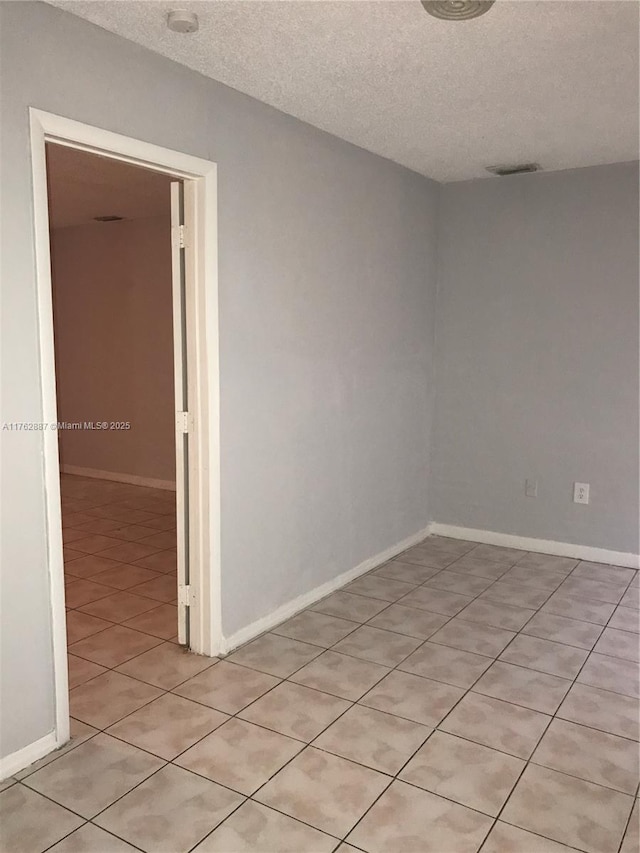 empty room with visible vents, a textured ceiling, and baseboards