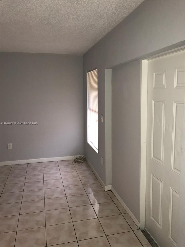 spare room featuring baseboards, a textured ceiling, and light tile patterned flooring