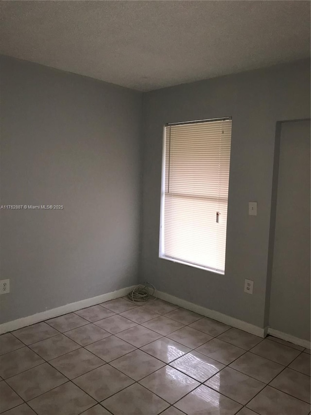 unfurnished room featuring light tile patterned floors, baseboards, and a textured ceiling