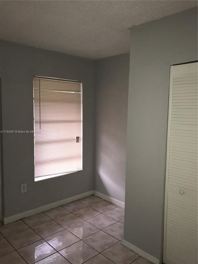 empty room featuring light tile patterned floors, a textured ceiling, and baseboards