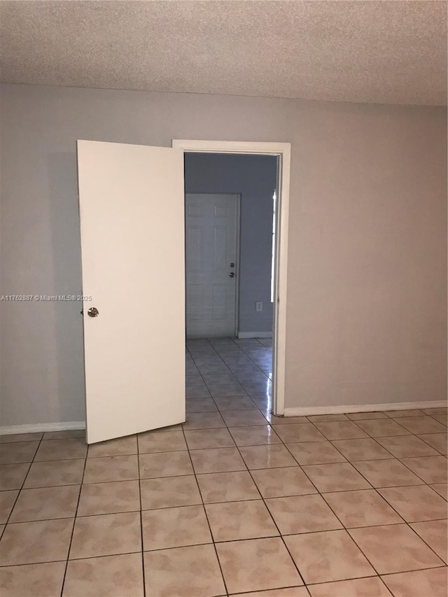 spare room with light tile patterned flooring, a textured ceiling, and baseboards