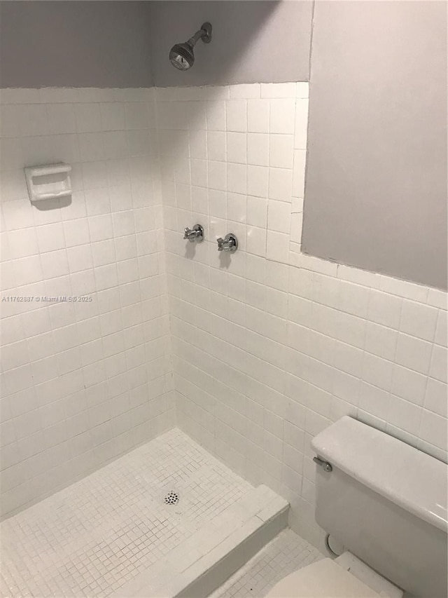 full bath featuring a wainscoted wall, tile walls, toilet, and a stall shower